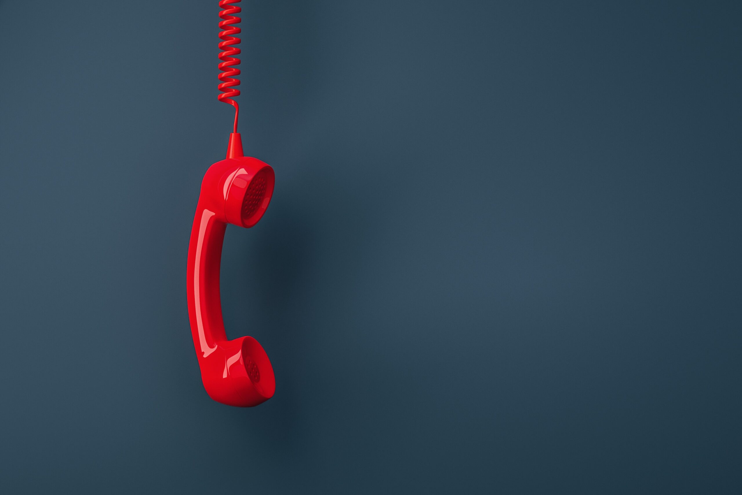 Red landline telephone handset hanging by its cord